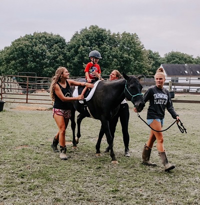 A boy riding a horse while two women support him on either side. A third woman leads the horse.