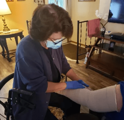 A COTA wearing a mask and gloves bandages a client's leg.
