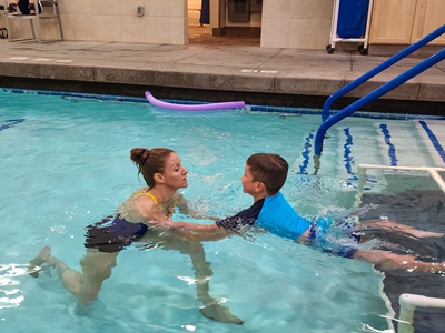 An OTR supports a child's arms as he floats in a swimming pool.