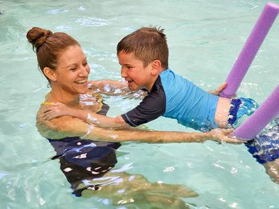 An OTR holds a pool noodle across a child's waist as he floats in a pool.