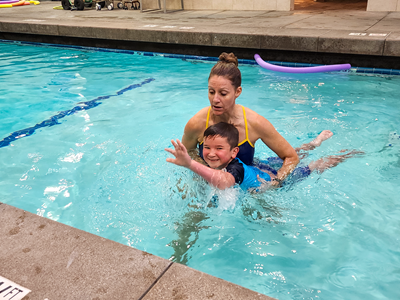 An OTR supports a child around the waist as he learns to swim.